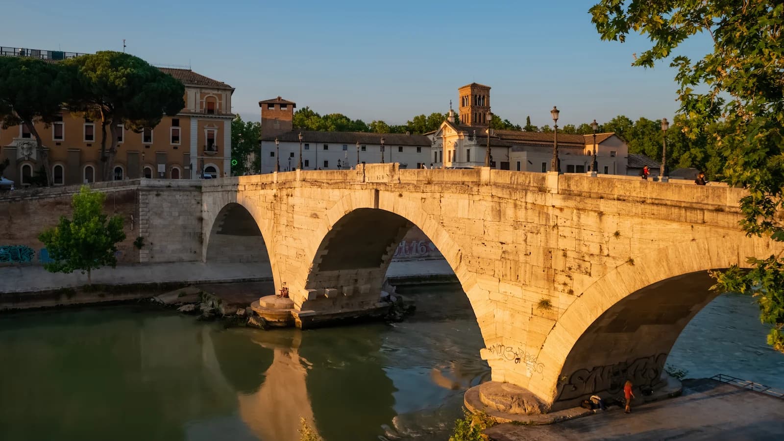 Ponte Fabricio, the ancient bridge connecting the Tiber Island to the Jewish Quarter in Rome, reflected in the Tiber River at sunset.