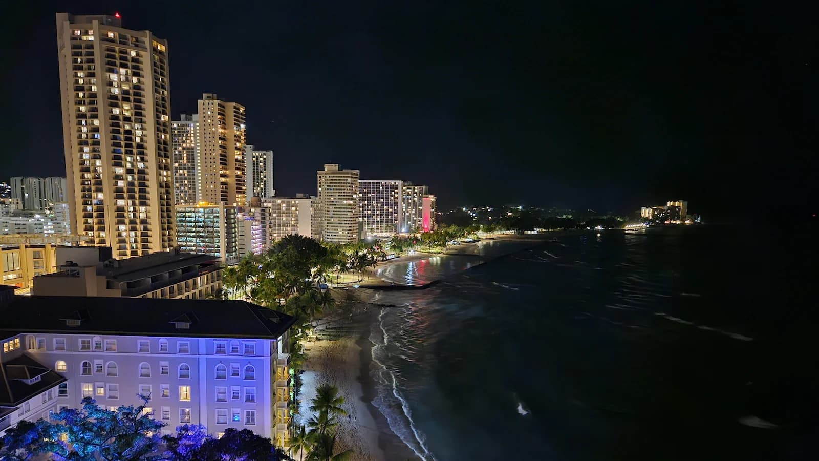 Vibrant nighttime view of Waikiki Beach and skyline from the historic Moana Surfrider Hotel, base for Essential History Expeditions’ Pearl Harbor at 85 history and culture tour.