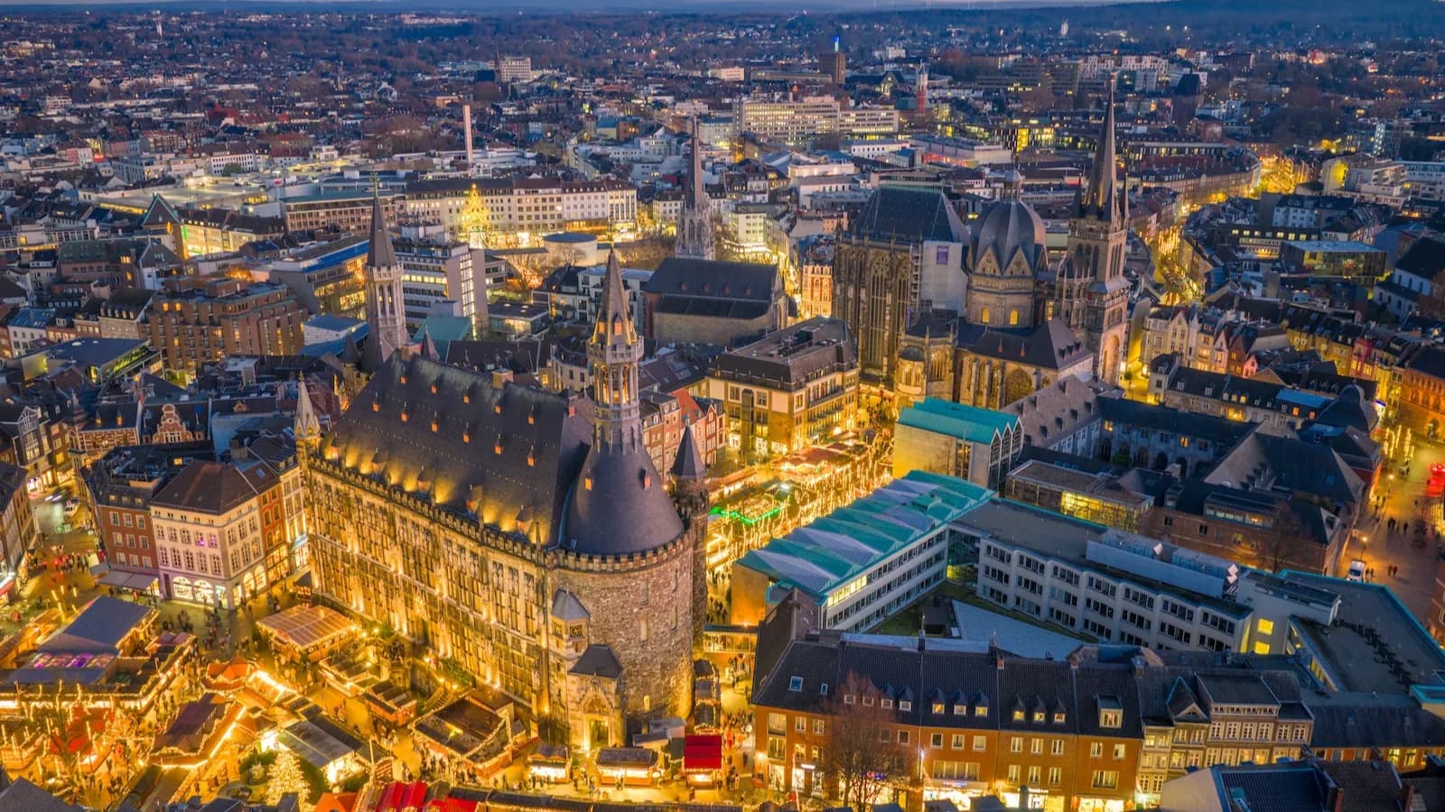 Aachen Christmas Market at dusk with the illuminated historic City Hall and Cathedral. Guests on our Bulge 85 tour enjoy this top-ranked European Christmas market in December 2029.